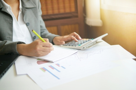 Business woman hand writing note finance analysis work with calculator checking data in officeの写真素材