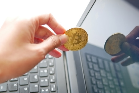 Hand holding cryptocurrency golden bitcoin coin from laptop screen. Conceptual image for virtual currency business from computer network.の写真素材