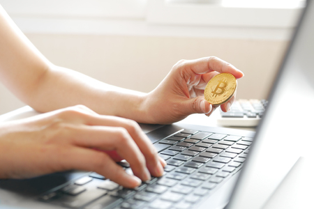 Hand holding cryptocurrency golden bitcoin coin in front of laptop screen. Conceptual image for virtual currency business from computer network.の写真素材