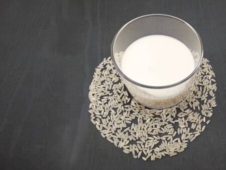 Glass of rice milk, with rice grains. On gray rustic wooden backgroundの写真素材