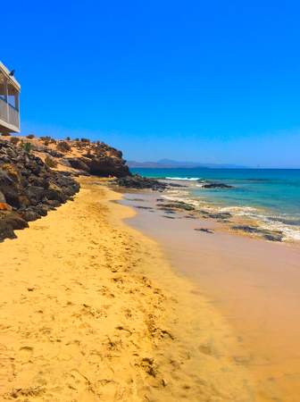 sandy and rocky bay on Fuerteventura, one of the canary islands, with a building on the cliffの写真素材