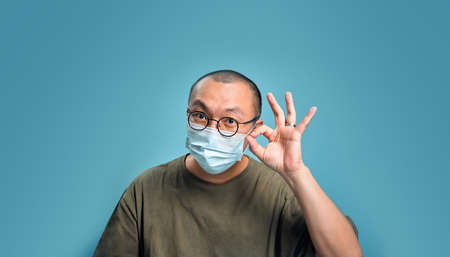 Young asian man wearing respirator mask to protect virus outbreak and feeling positive on blank background. New virus outbreak that alert the world health concept, Empty space isolated on blue.の写真素材