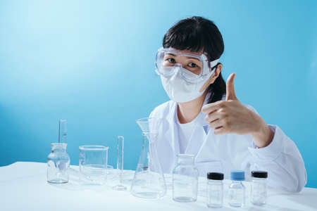Smart young asian female scientist in lab coat with Medical face mask show confident. Empty space in studio shot isolated on colorful blue background. Medical concept.の写真素材