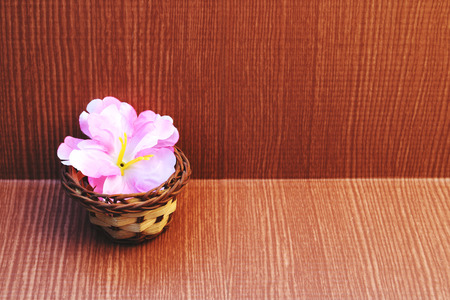 Pink artificial flower is in the small basket on wooden backgroundの写真素材