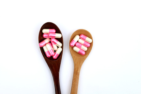 white and pink capsules in two wooden spoonsの写真素材