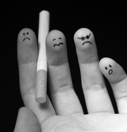 Black and white photo of fingers holding cigarette. Sad smiley painted on fingertips. Conception of addiction and anti-smoking.の写真素材