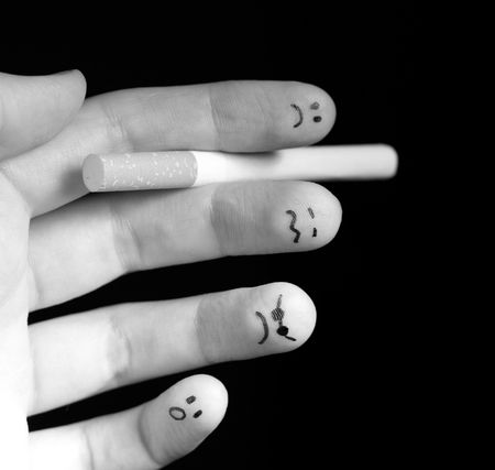 Black and white photo of fingers holding cigarette. Sad smiley painted on fingertips. Conception of addiction and anti-smoking.の写真素材