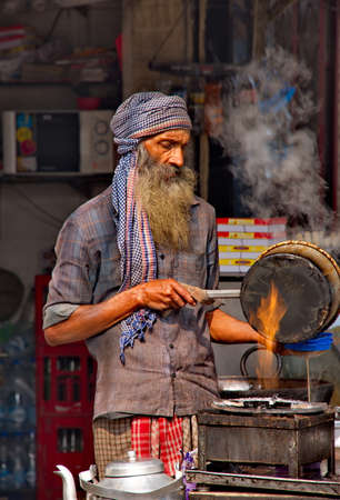 DELHI. INDIA. January 30, 2016. A brutal Hindu with a beard in pagri prepares local masala tea on an open fire in the city marketのeditorial素材