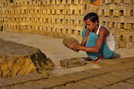 Assam. India February 08, 2016. A small brick factory. A young man uses a mold to make bricks out of clay and lay them out in the sun to dry.のeditorial素材