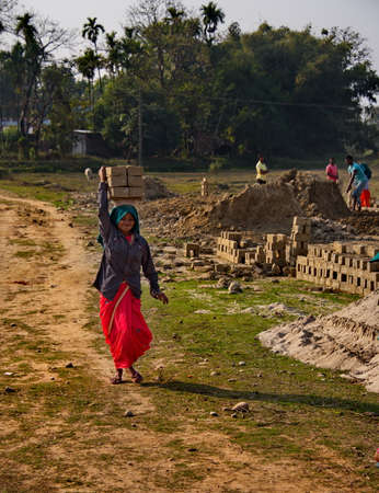 Assam. India February 08, 2016. A small brick factory. Young girls carry 8 dried clay bricks on...