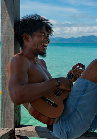 Semporna. Malaysia. November 30, 2018. A young resident of the island of Borneo plays the guitar and sings songs on the pier of the fishing village of sea gypsies, located on the shore of a reef islanのeditorial素材