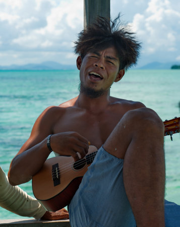 Semporna. Malaysia. November 30, 2018. A young resident of the island of Borneo plays the guitar and sings songs on the pier of the fishing village of sea gypsies, located on the shore of a reef islanのeditorial素材