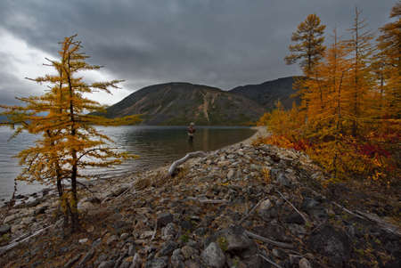 Russia. Far East, Magadan region. September 06, 2018. A lone fisherman surrounded by autumn colors is fishing on a spinning rod on the shore of the relict Lake Maxi.のeditorial素材