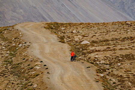 Khorog. Tajikistan. August 10, 2019. A lone tourist with a bicycle in his hands goes uphill along a high-altitude dilapidated road on the most difficult section of the Pamir highway.のeditorial素材