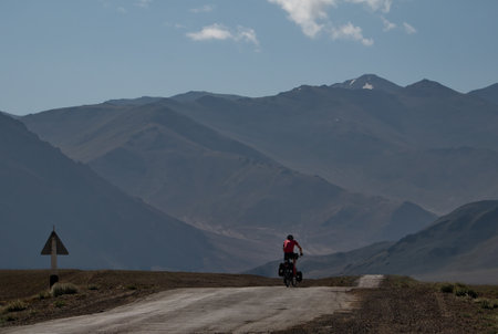 Khorog. Tajikistan. August 11, 2019. A lone tourist on a bicycle rides along a high-altitude ramshackle road on the most difficult section of the Pamir highway.のeditorial素材