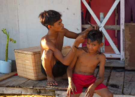 Mobul. Malaysia. December 02, 2018. A young boy from a Gypsy village of fishermen cuts a little boy's hair on the doorstep of his house.のeditorial素材