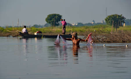 Mandalay. Myanmar. November 21, 2016. A young fisherman in a straw hat sets up a net on Lake...