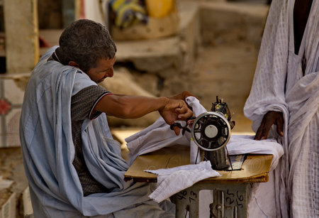 Nouakchott. Mauritania. October 03, 2021. A tailor sews a dress on a sewing machine on the street under the scorching sun. Traditionally, all Mauritanians wear the national clothes of the boubou.のeditorial素材