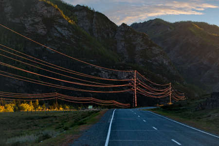Russia. The South of Western Siberia, the Altai Mountains. High-voltage wires illuminated by sunset light against the background of shaded mountains along the Chui tract.の写真素材