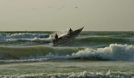 Saint-Louis. Senegal. October 11, 2021. Every day at dawn fishermen on long wooden boats go out to sea fishing with difficulty overcoming coastal waves.のeditorial素材