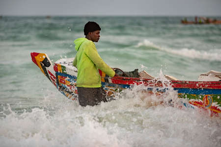 Nouakchott. Mauritania. October 03, 2021. A young fisherman from a coastal village in the early morning is preparing for another trip to the sea standing next to a large wooden boat.のeditorial素材
