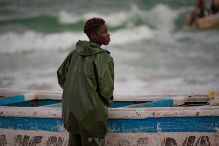 Nouakchott. Mauritania. October 03, 2021. A young fisherman from a coastal village in the early morning is preparing for another trip to the sea standing next to a large wooden boat.のeditorial素材