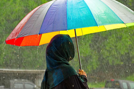 Malaysia. Sandakan. A girl in national Muslim clothes under a torrential tropical rain walks with an...