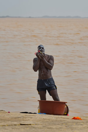 Saint-Louis. Senegal. October 10, 2021. A young muscular resident of an African city washes on the sandy shore of the Senegal River on the city embankment.のeditorial素材