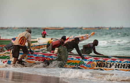 Nouakchott. Mauritania. October 03, 2021. A group of fishermen in special protective clothing made of rubber fabric launch a large fishing boat on the sandy shore of the Atlantic Oのeditorial素材