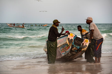 Nouakchott. Mauritania. October 03, 2021. A group of fishermen in special protective clothing made of rubber fabric launch a large fishing boat on the sandy shore of the Atlantic Oのeditorial素材