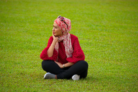 Kuala Lumpur. Malaysia. November 24, 2018. Portrait of a young woman in a colored shawl sheila (the loosest headdress of Muslim women) sitting on the grass in the park of the Sultaのeditorial素材