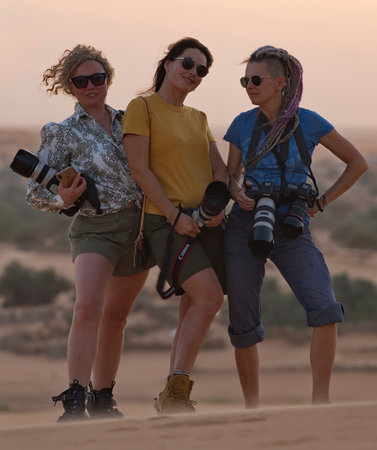 Shingetti. Mauritania. October 05, 2021. Portrait of three young female tourists with professional cameras posing against the sunset in the Sahara Desert.のeditorial素材