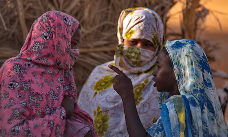 Shingetti. Mauritania. 05 October 2021. Three young African girls in national multicolored headscarves are violently discussing everyday problems of village life in the sands of thのeditorial素材