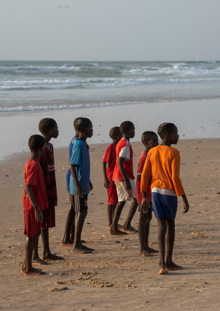 Saint-Louis. Senegal. October 11, 2021. A group of African boys are closely watching the stormy activity of the townspeople on the sandy beach near the sea market.のeditorial素材