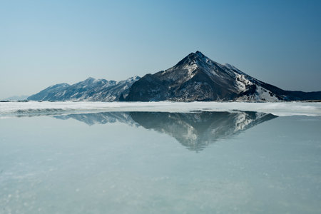 Russia. Far East, Sakhalin Island. View of an extinct volcano surrounded by spring ice on the shore of the Tikhaya Bay of the Gulf of Patience in the Sea of Okhotsk.の写真素材