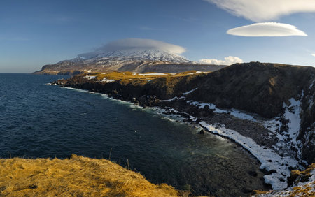 Russia. Kuril Islands. Panorama of the high steep coast of the Sea of Okhotsk on the island of Iturup at the foot of snow-capped volcanoes.の写真素材