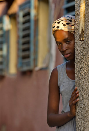 Joel, Senegal. October 15, 2021. Portrait of a confused young African girl hiding around the corner of the house.のeditorial素材