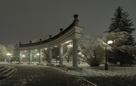 Novokuznetsk, Russia. November 01 2024. The colonnade around the central fountain of the in City Park, covered with the first autumn snow and illuminated by lanterns of cold light.の写真素材