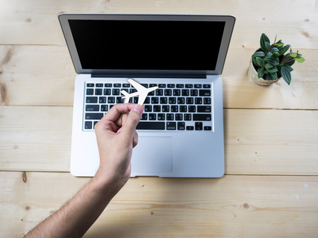 Air plane symbol holding by hand with computer notebook on wooden tableの写真素材