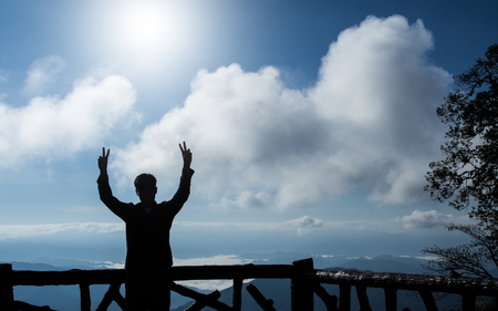 silhouette of man making peace gesture two hands, mountain and sky backgroundの写真素材