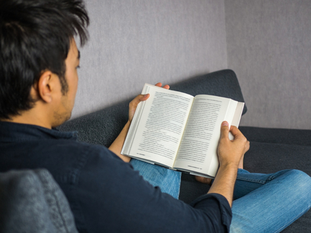Man reading book on sofa at homeの写真素材