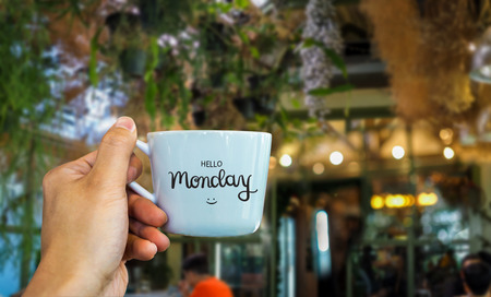 Hello Monday text on coffee mug hand holding in cafeの写真素材