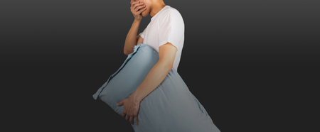 Man yawning holding a pillow with black gradient backgroundの写真素材