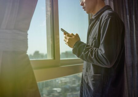 Man using phone and standing by the windowの写真素材