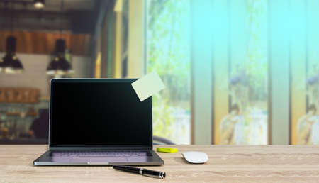 Computer laptop with empty sticky note on wooden desk in a cafe in the backgroundの写真素材