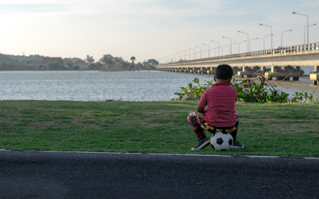 The children sit on the football in the park, with views of the lake.の写真素材