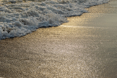 Close up shot of waves breaking on the sandy beach at sunriseの写真素材