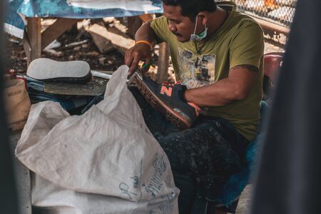 Songkhla, Thailand, May 1, 2018 : Unknown Shoemaker repairing a shoe sole on pathway beside traffic road near HatYai Railway Station, Hatyai, Sonkhla, Thailand.のeditorial素材
