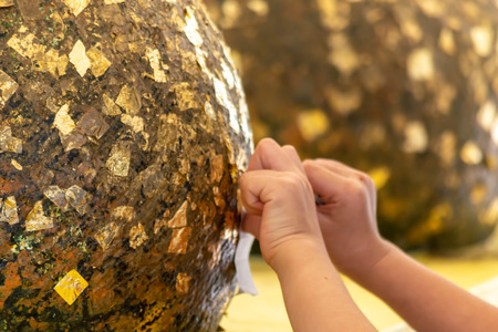 The girl's hand hand put a Gold leaf on the stone ball backgroundの写真素材