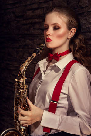 Beautiful girl with saxophone in a white shirt and red suspendersの写真素材